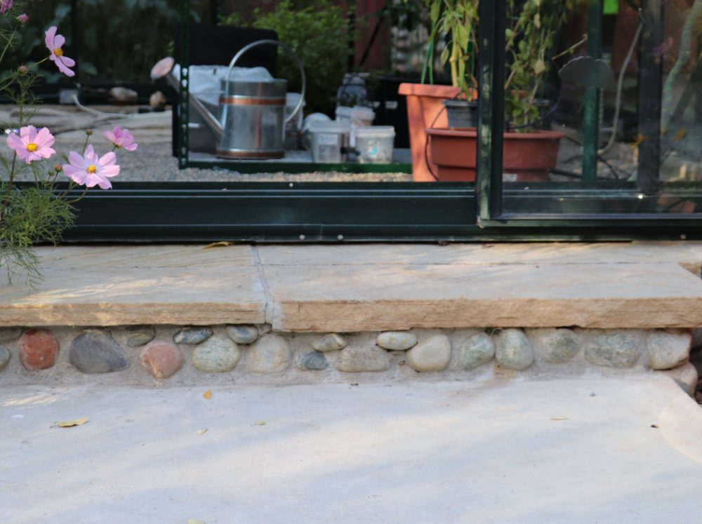 Natural stone greenhouse foundation covered with a concrete slab. 