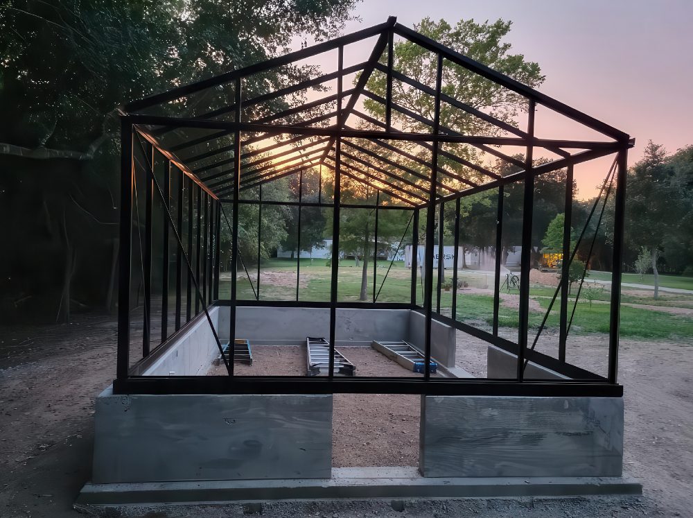 Exterior of a greenhouse under construction at dusk. 