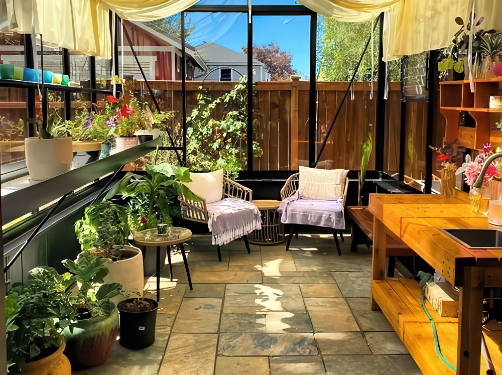 Glass gable greenhouse interior with floating shelves to the left, a potting station with sink to the right and two lounging chairs at the back.