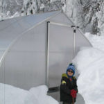 Gothic arch shaped greenhouse with loads of snow around and a person standing in front of it