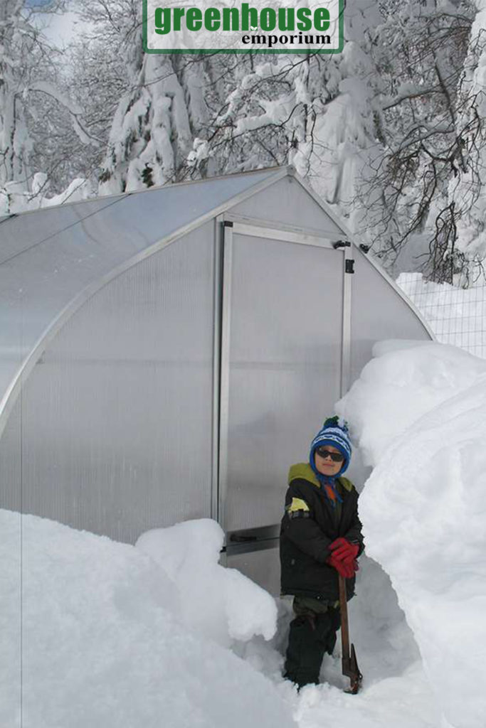 Gothic arch shaped greenhouse with loads of snow around and a person standing in front of it