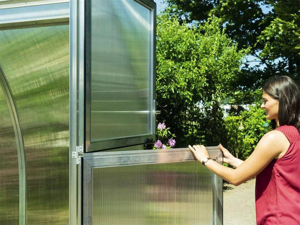 A woman opening the bottom section of the door of the Arcus Greenhouse