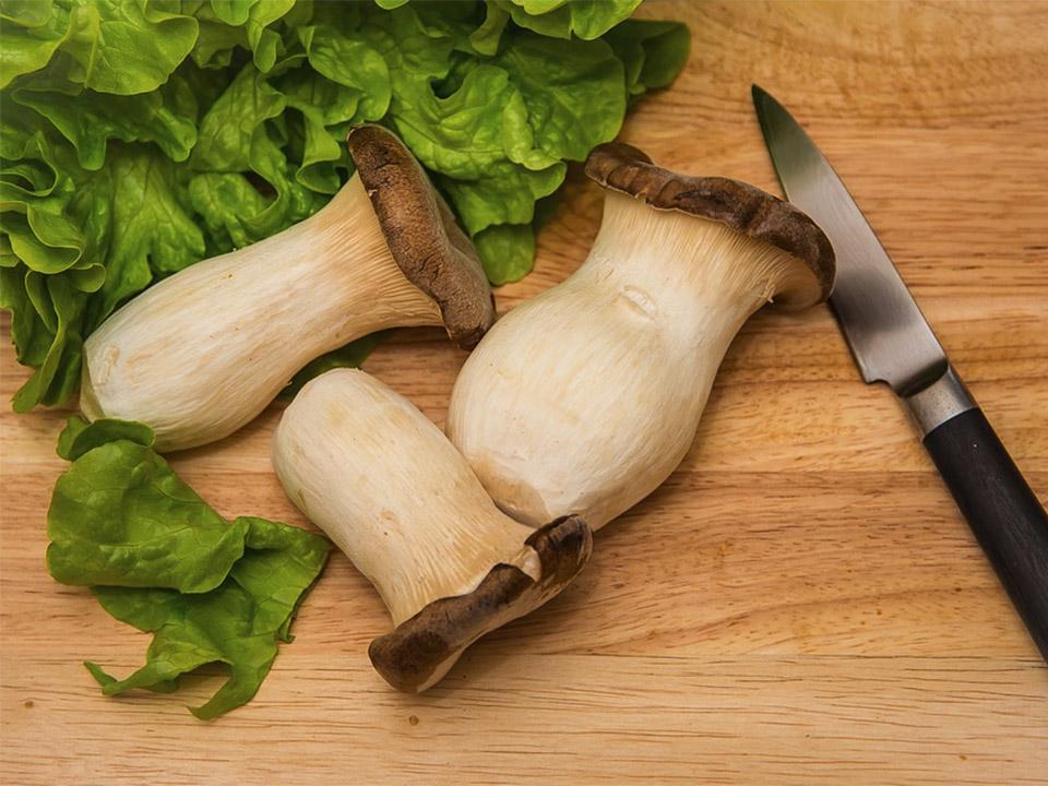 Three ready to cook oyster mushrooms with green leafy vegetables on the left side and a knife on the right side