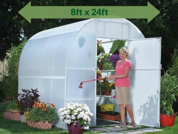 Solexx  8ft x 24ft Gardener's Oasis Greenhouse G-224 - open door - with plants inside - green arrow on top showing dimensions - a woman by the door watering the plants