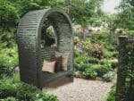 The Adelaide Dove Gray Arbor With Bench and Pillows in a garden