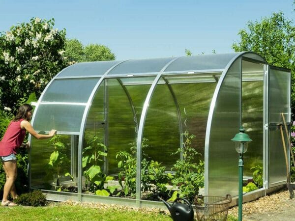 Side view of Arcus 3 Greenhouse - open door - The two side panels are fully opened - a woman opening the third side panel