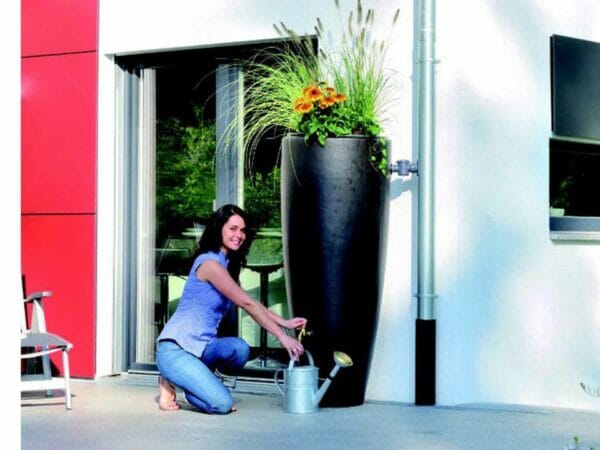 A woman pouring water from the Bullet Rain Barrel with Planter.