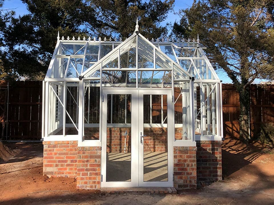 EOS Royal Victorian Antique Orangerie, white frame, freshly constructed on brick stem wall shown with one roof window open, door closed