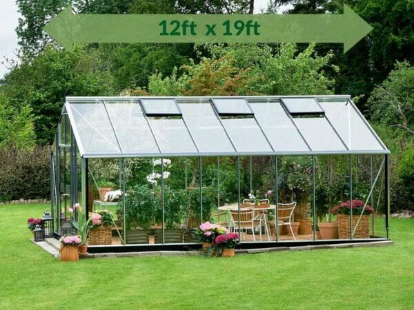 Juliana Gardener Greenhouse 12ft x 19ft - 3mm toughened glass - side view - green arrow on top showing dimensions - in a garden