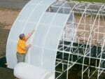 A man installing Solexx Greenhouse Covering Rolls to a greenhouse