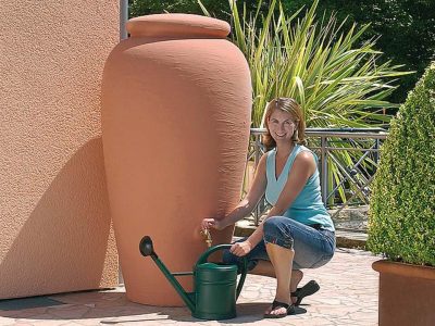 A woman on the right side pouring water from the Venetia Rain Barrel with Planter