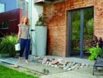 Wave Barrel & Planter Outdoor. A woman holding a sprinkler on the left side.