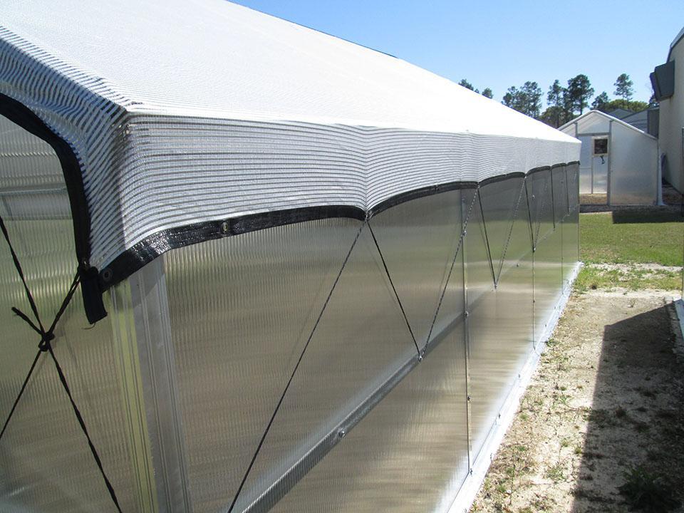 White external shade cloth strapped over a greenhouse