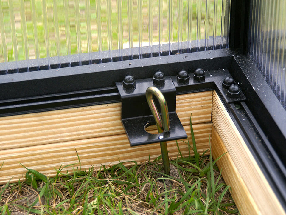 Ground anchor attached to a greenhouse on a wooden foundation