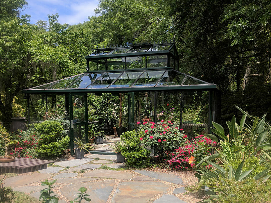 Garden setting with a large glass greenhouse with plants and trees growing inside