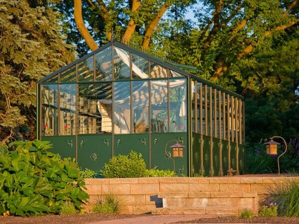 Retro Royal VI36 4mm glass greenhouse with green frame, decorative panels, shown highlighted by sunset, shade curtains installed on interior