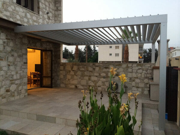 Grey Selt System Sunbreaker 400 Pergola, side view, slats in open position, structure above stone patio area