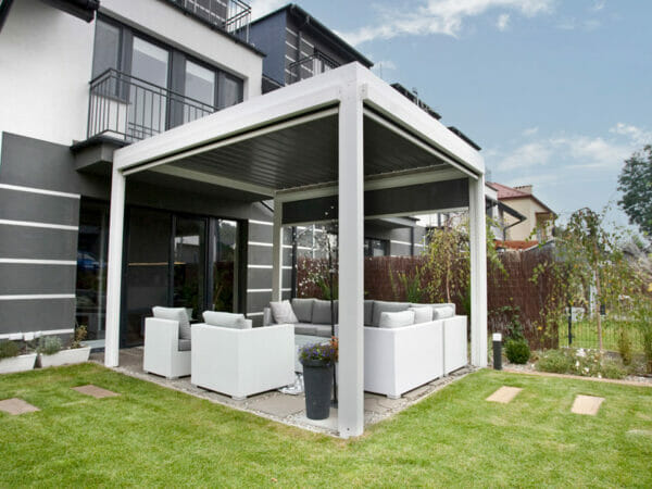 White Selt System Sunbreaker 400 Pergola, side view, lawn with patio and pergola installed above outdoor furniture setting, slats in closed position