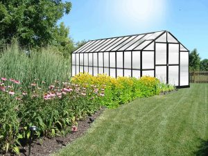 Exterior front and side view Monticello Growers 8x24, black frame, polycarbonate panels, doors closed, flower garden setting
