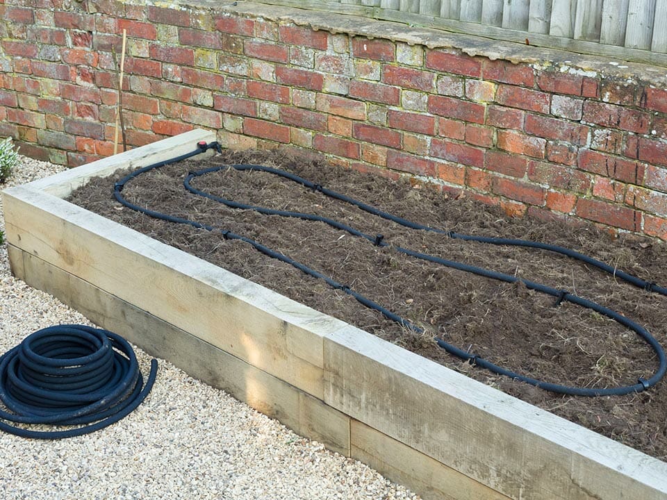 Exterior planting bed filled with soil, soaker hose on top of soil