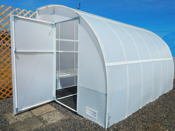 Exterior view of arched lean-to greenhouse against trellis board, door open, empty wire shelving visible in interior
