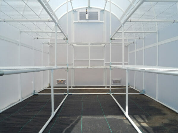 Interior view of arched greenhouse, facing rear or greenhouse, shelving on both sides, two vents visible in lower corners of rear wall