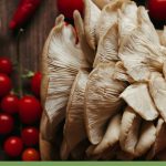 Close up of edible mushroom with tomatoes on wooden cutting board with text: How Do I Grow Mushrooms in a Greenhouse?