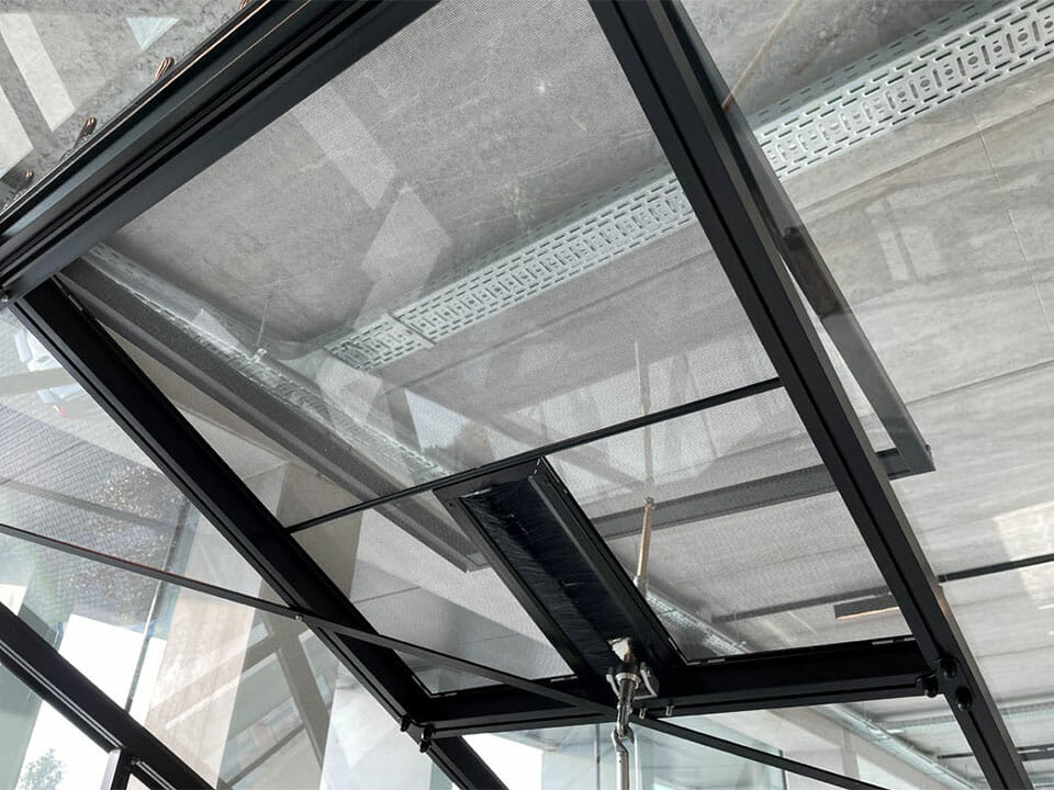 Fly screen installed in a roof window of a black framed Janssens Greenhouse - View from the inside of the greenhouse