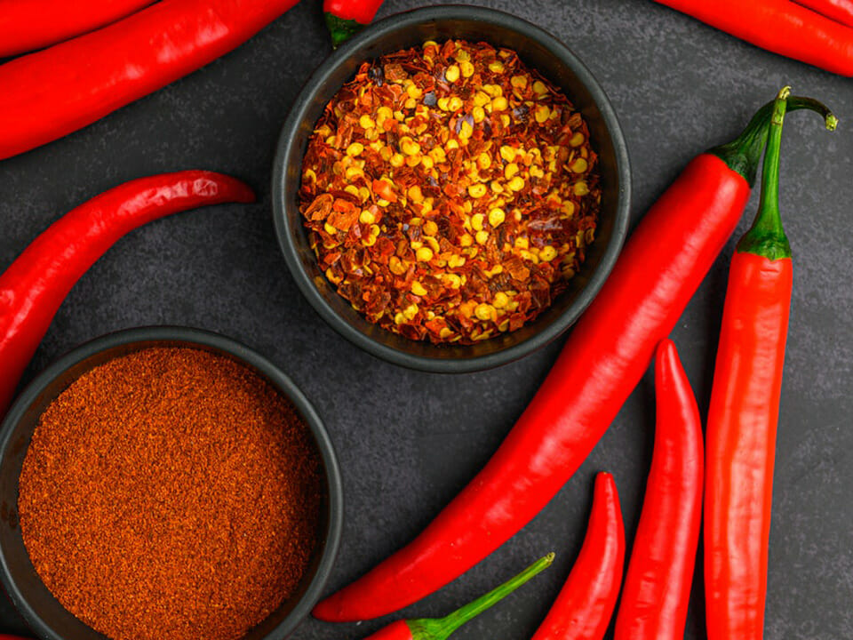 Chili powder, chili flakes, and red hot chili peppers on a black surface