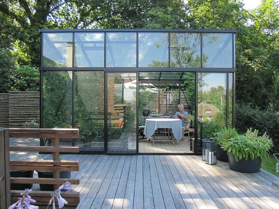 Janssens Modern Glass Greenhouse in a backyard on a wooden deck