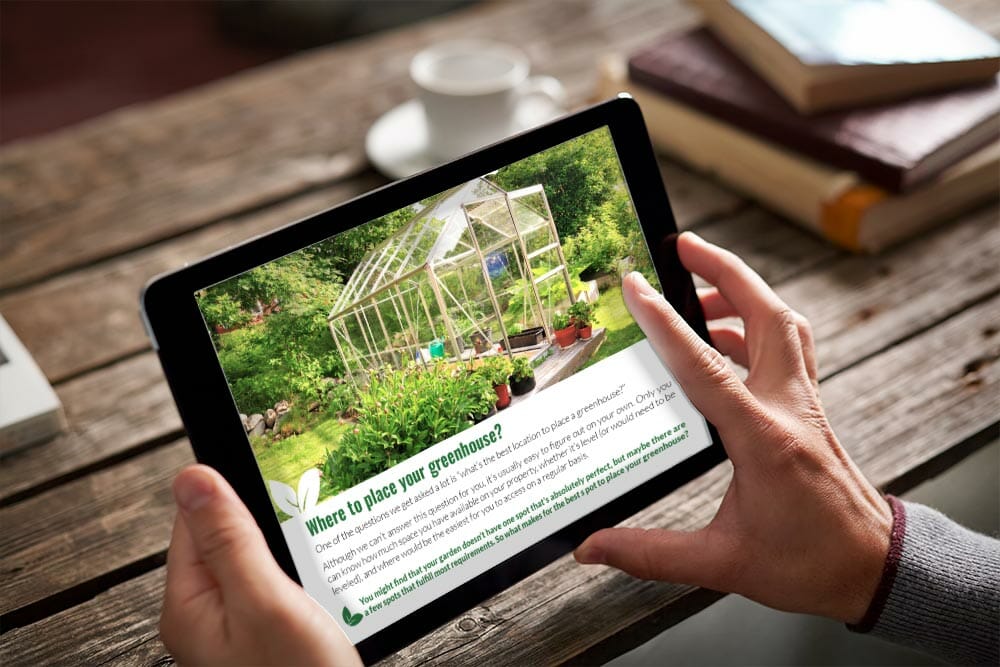 Tablet held in hands over a wooden table with books, document on tablet is a page of the eBook: Your Greenhouse, Your Choice - A Practical Guide To Picking Your Greenhouse Kit
