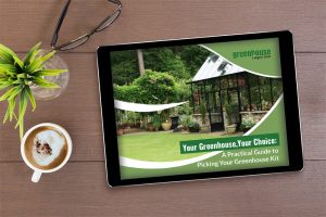 Tablet on a table with plant, coffee, and glasses, on the table is the cover of the eBook: Your Greenhouse, Your Choice - A Practical Guide To Picking Your Greenhouse Kit