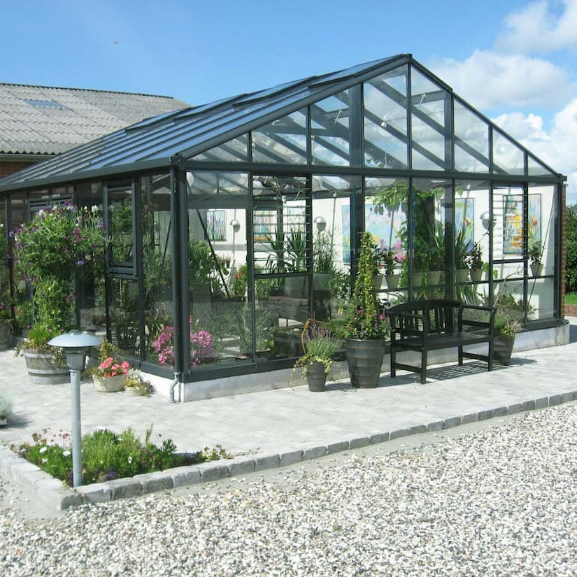 Large Janssens glass greenhouse with black frame close to a house