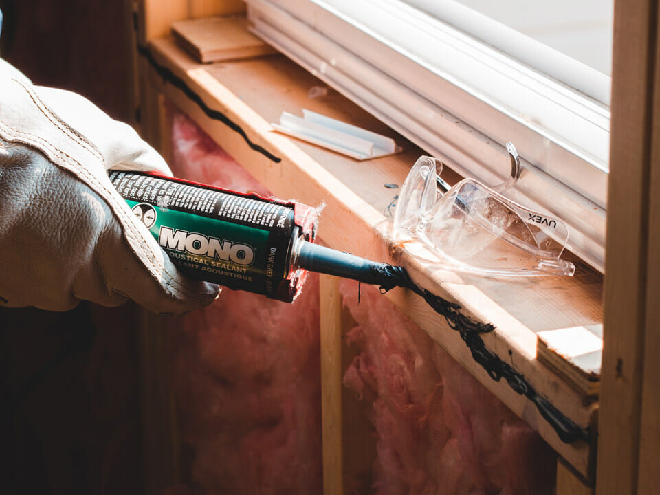Worker in gloves using caulk to close a crack under a window to improve insulation