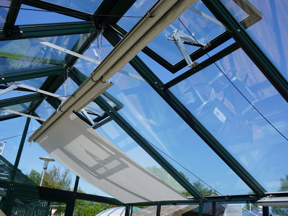 Top unit of the Retractable Roll-up Shade Curtains installed and partially unfurled in a greenhouse