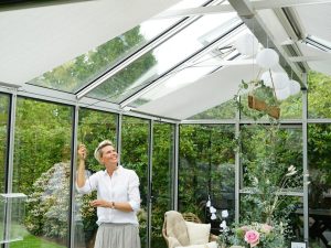 Woman activating top-mounted Retractable Roll-up Shade Curtains in a greenhouse