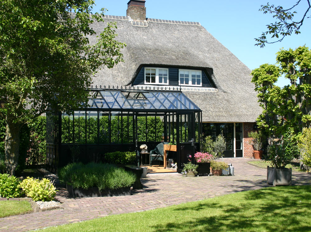 Exaco Janssens Retro Victorian Greenhouse in front of a classic house with thatched roof