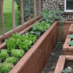 Interior of a greenhouse attached to a house with raised beds and the Greenhouse Emporium logo at the top.