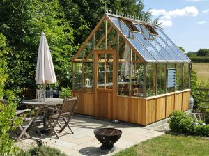 Alton Cheltenham Wooden Greenhouse in a backyard with a seating area in front