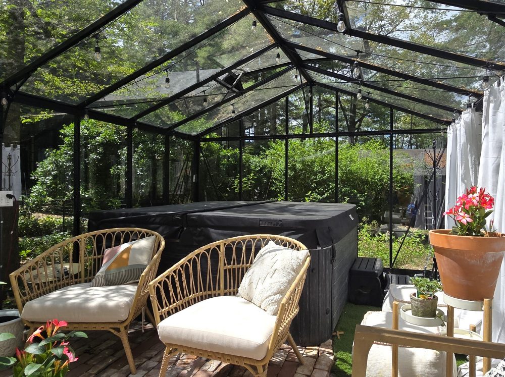 Luxurious greenhouse interior featuring a bubbling hot tub, surrounded by comfortable seating, elegant curtains, and ambient string lights.