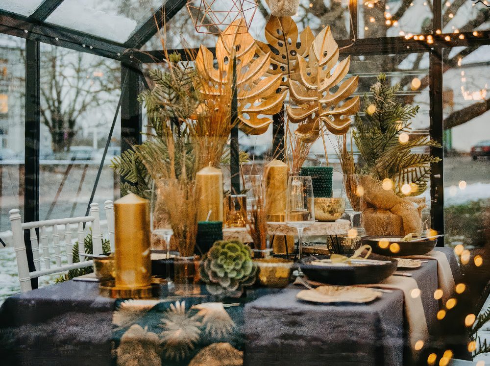 Greenhouse interior featuring a dining table beautifully decorated with twinkling lights, holiday decor, and greenery for a festive gathering.