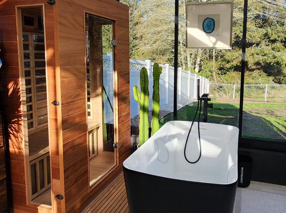 Luxurious black-framed greenhouse interior featuring a modern wooden sauna, with space for a freestanding tub, surrounded by natural light.