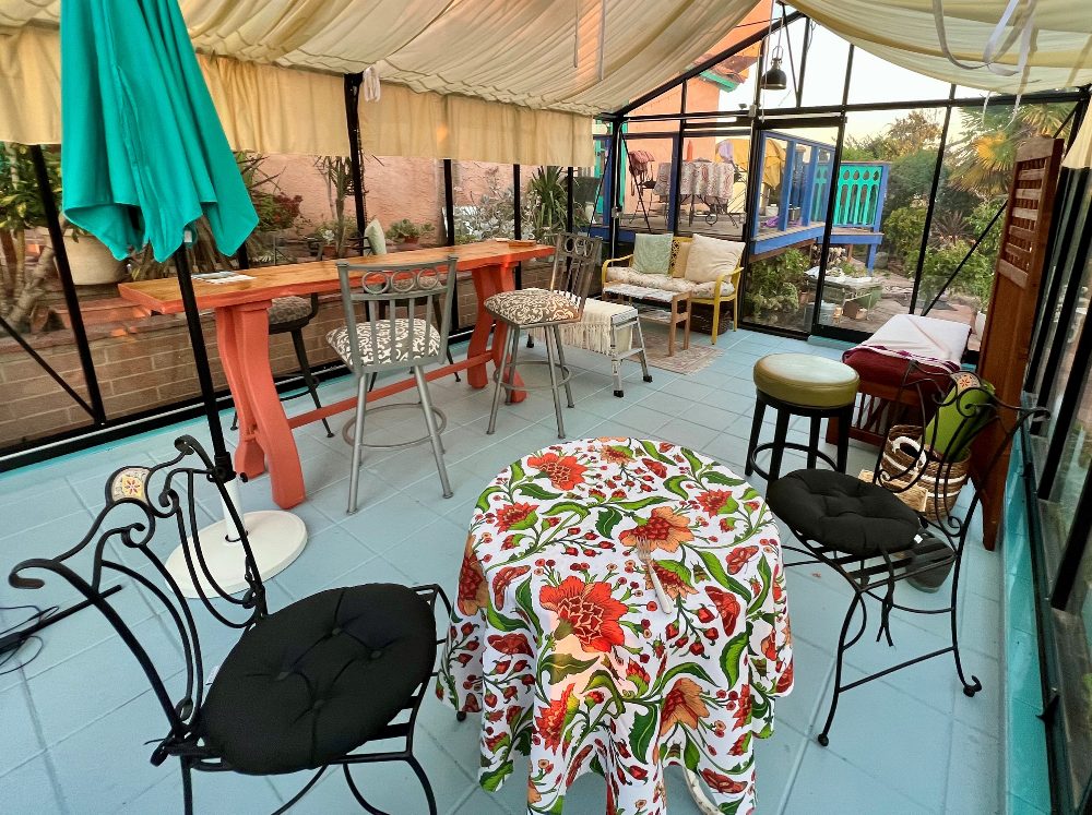 Greenhouse interior arranged as a festive party hosting area with various seating options, bistro tables, and overhead shade cloths.