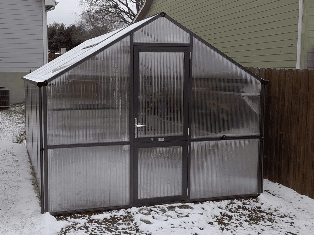 Front of Nelke Pro - the best greenhouse kit - set-up in a backyard by a fence covered in snow
