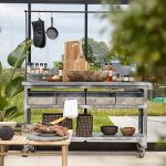 kitchen station set up inside of a greenhouse with sink and a small table next to it.