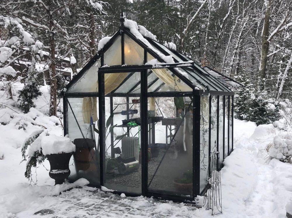 Small glass greenhouse in snow with a few heaters in it.
