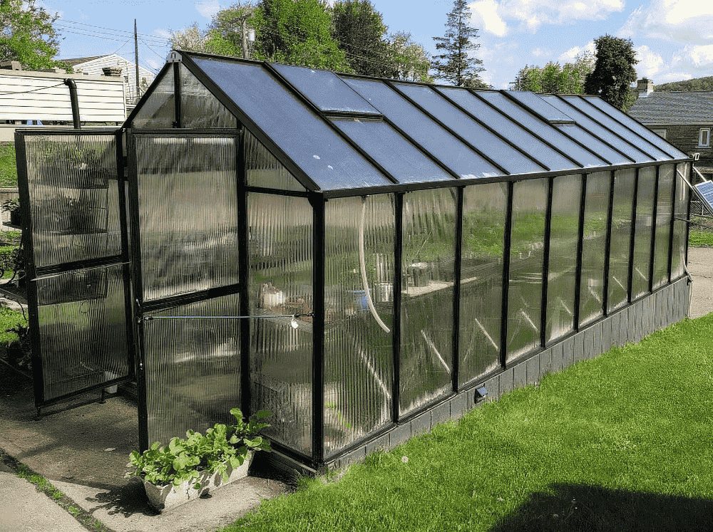 Front corner view of a MONT black framed polycarbonate greenhouse with the doors propped open. 