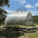 Exterior of a gothic arch polycarbonate Riga greenhouse on a hill with the Greenhouse Emporium logo at the top.