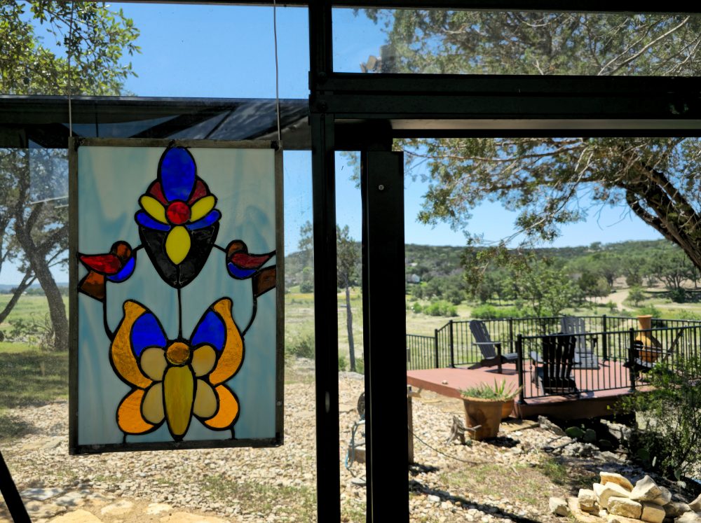 Stained glass butterfly and flowers hanging on a greenhouse wall.