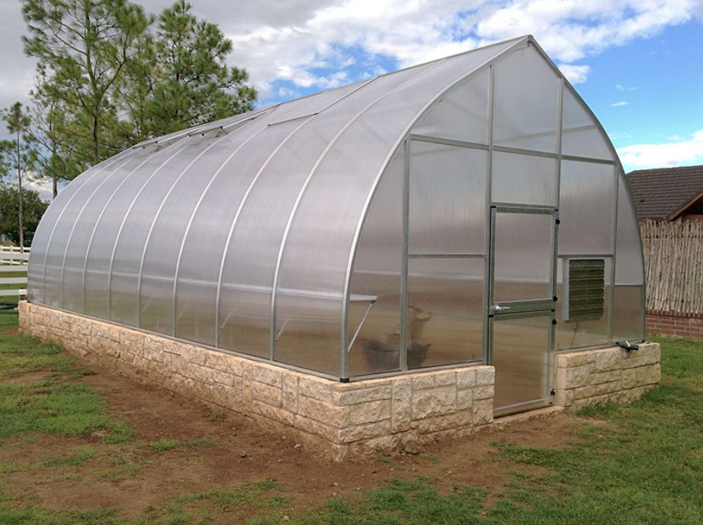 Front corner perspective of an extra large Riga 9 XL polycarbonate greenhouse with a stem wall and door extension kit.